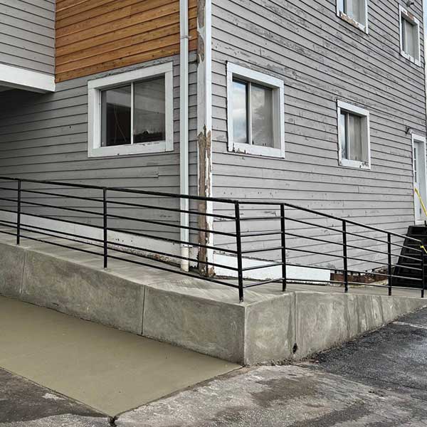 Concrete Access Ramp With Black Handrails Beside A Building.